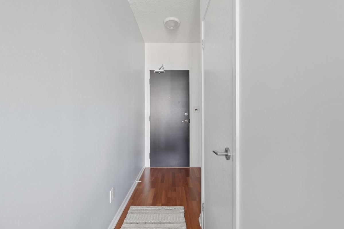 A hallway with a wooden floor, a white door, and a light switch on the wall.