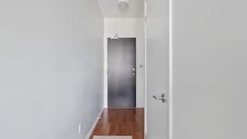 A hallway with a wooden floor, a white door, and a light switch on the wall.