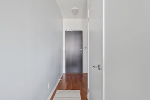 A hallway with a wooden floor, a white door, and a light switch on the wall.