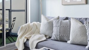 Una sala moderna con un sofá gris, una manta blanca y un control remoto sobre una mesita.