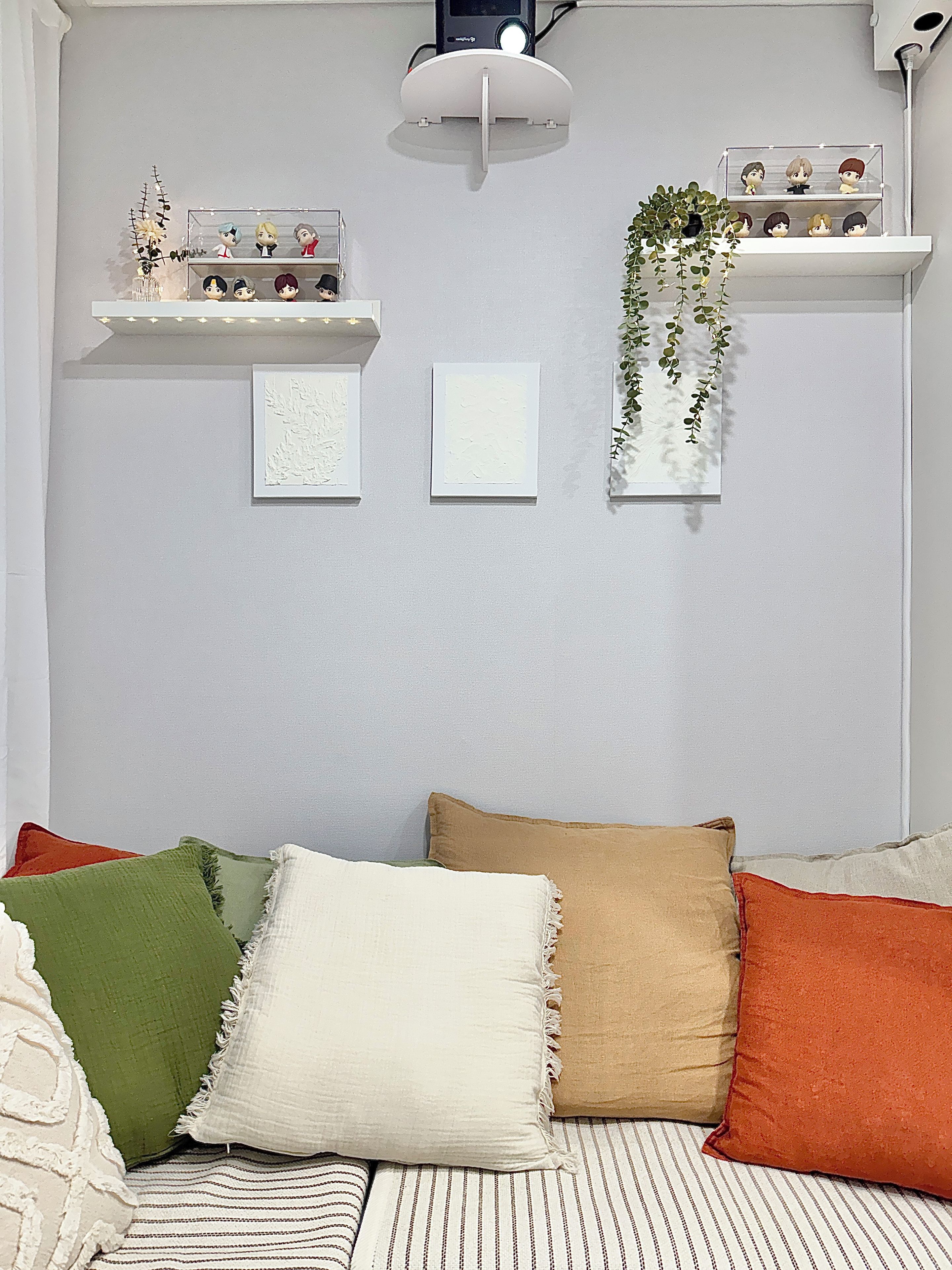A room with a sofa, pillows, wall-mounted shelves with figurines, and framed artwork.