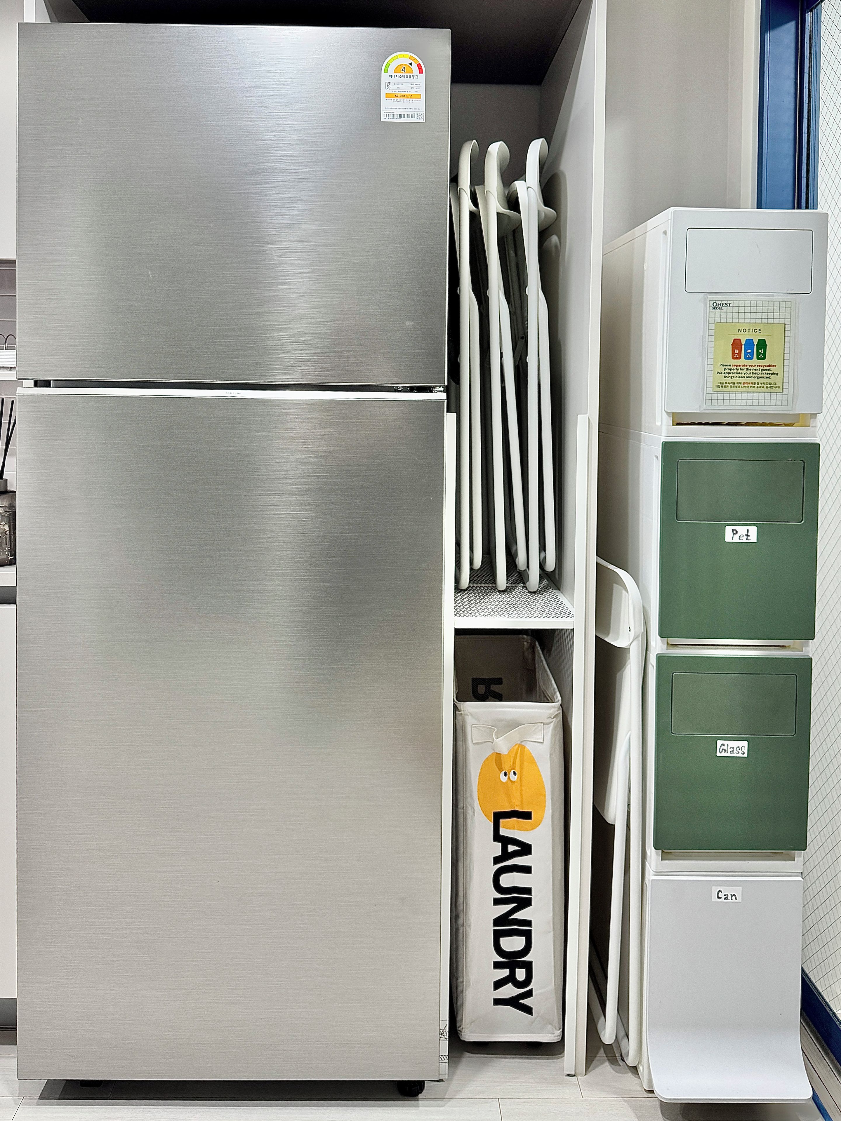 A stainless steel refrigerator, a laundry basket, and a recycling bin in a kitchen.