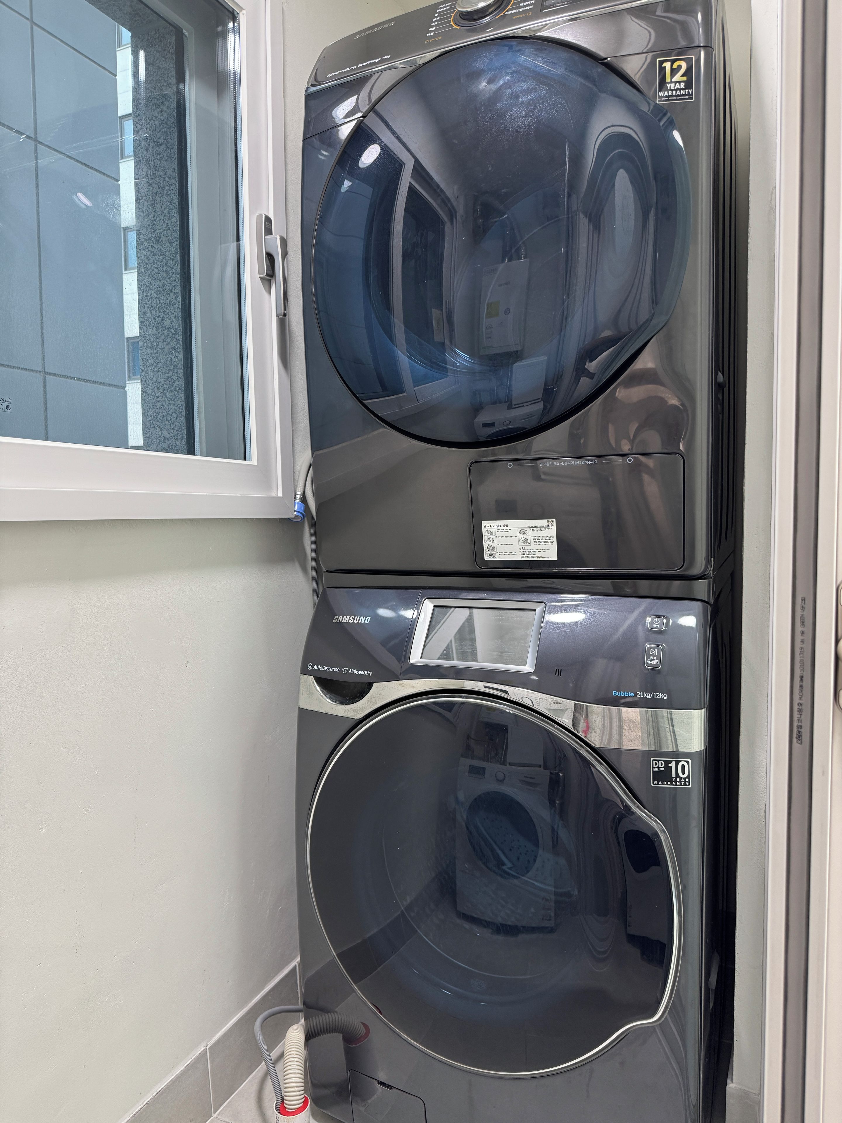 A Samsung front-loading washer and dryer unit with a 12-year warranty sticker, a control panel, and a hose connected to the unit.