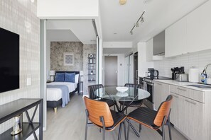 A modern kitchen with a dining area, a bedroom with a large bed and a nightstand, and a TV on the left. - Stunning Family-Friendly Parking & City Views! | Parking Available (Toronto)