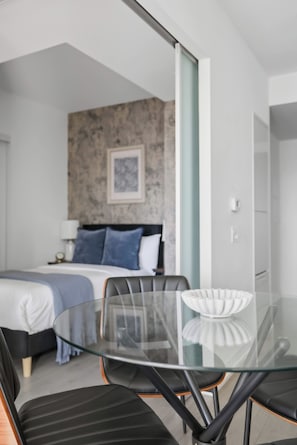 A modern hotel room with a glass dining table, black chairs, a bed with a blue headboard, and a framed picture on the wall. - Stunning Family-Friendly Parking & City Views! | Parking Available (Toronto)