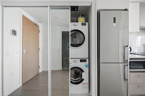 A laundry room with a stacked washer and dryer, a refrigerator, and a door with a 'Home Sweet Home' sign. - Stunning Family-Friendly Parking & City Views! | Parking Available (Toronto)