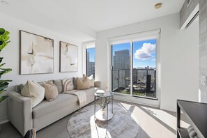 A modern living room with a sofa, a coffee table, and a large window with a city view. - Stunning Family-Friendly Parking & City Views! | Parking Available (Toronto)
