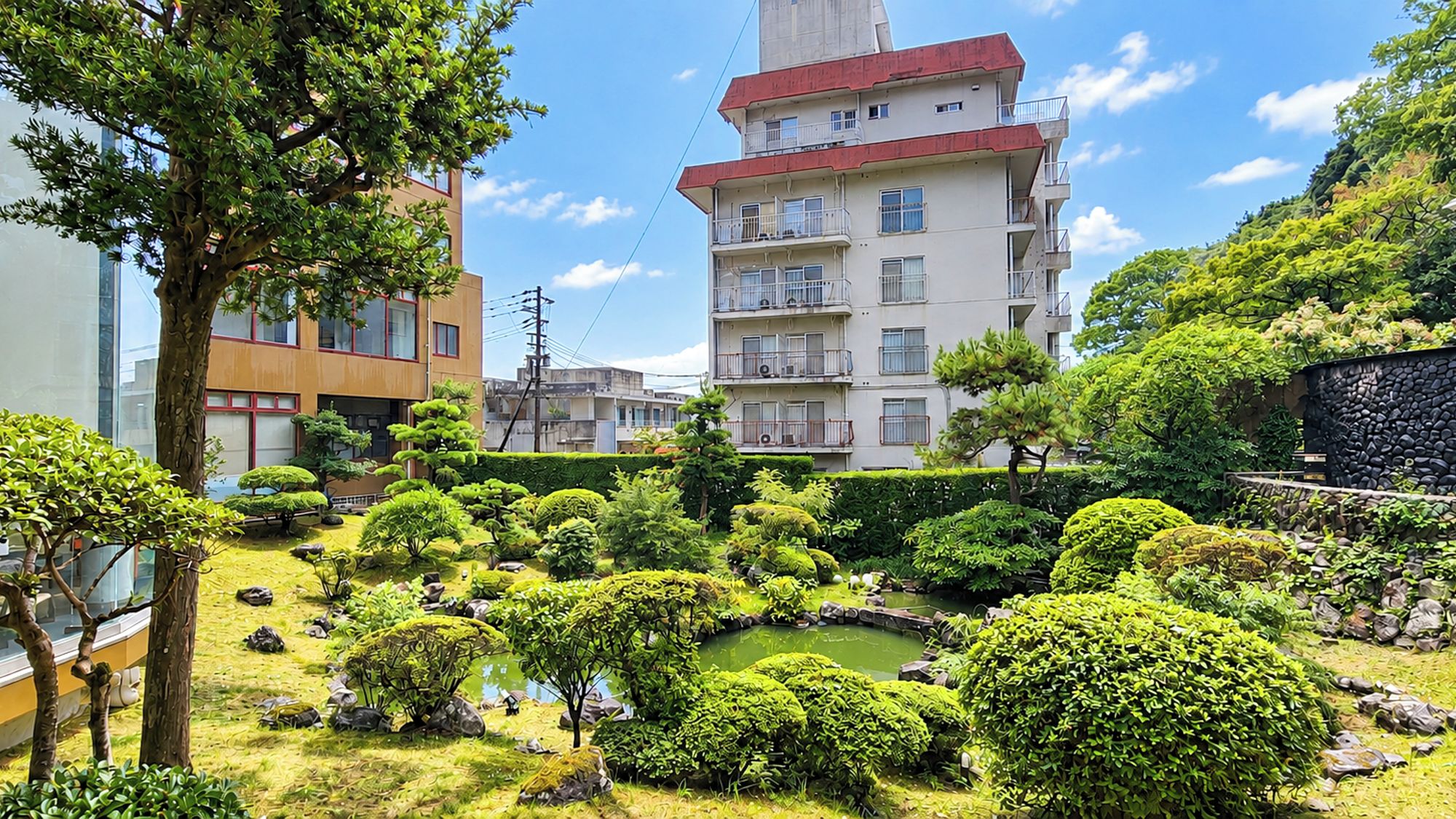 A landscaped garden with various shrubs and a small pond, surrounded by residential buildings.