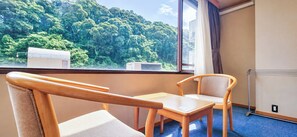 Quarto com vista para uma floresta, janela com cortinas, radiador e mesa com cadeiras.