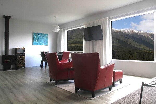 A modern living room with a large window, red chairs, a flat-screen TV, and a fireplace.