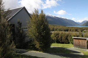 A rustic building with a sloped roof, surrounded by dense greenery and a mountainous backdrop.