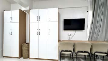 A modern room with a white wardrobe, a flat-screen TV, and a sofa with chairs.