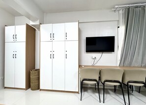 A modern room with a white wardrobe, a flat-screen TV, and a sofa with chairs.