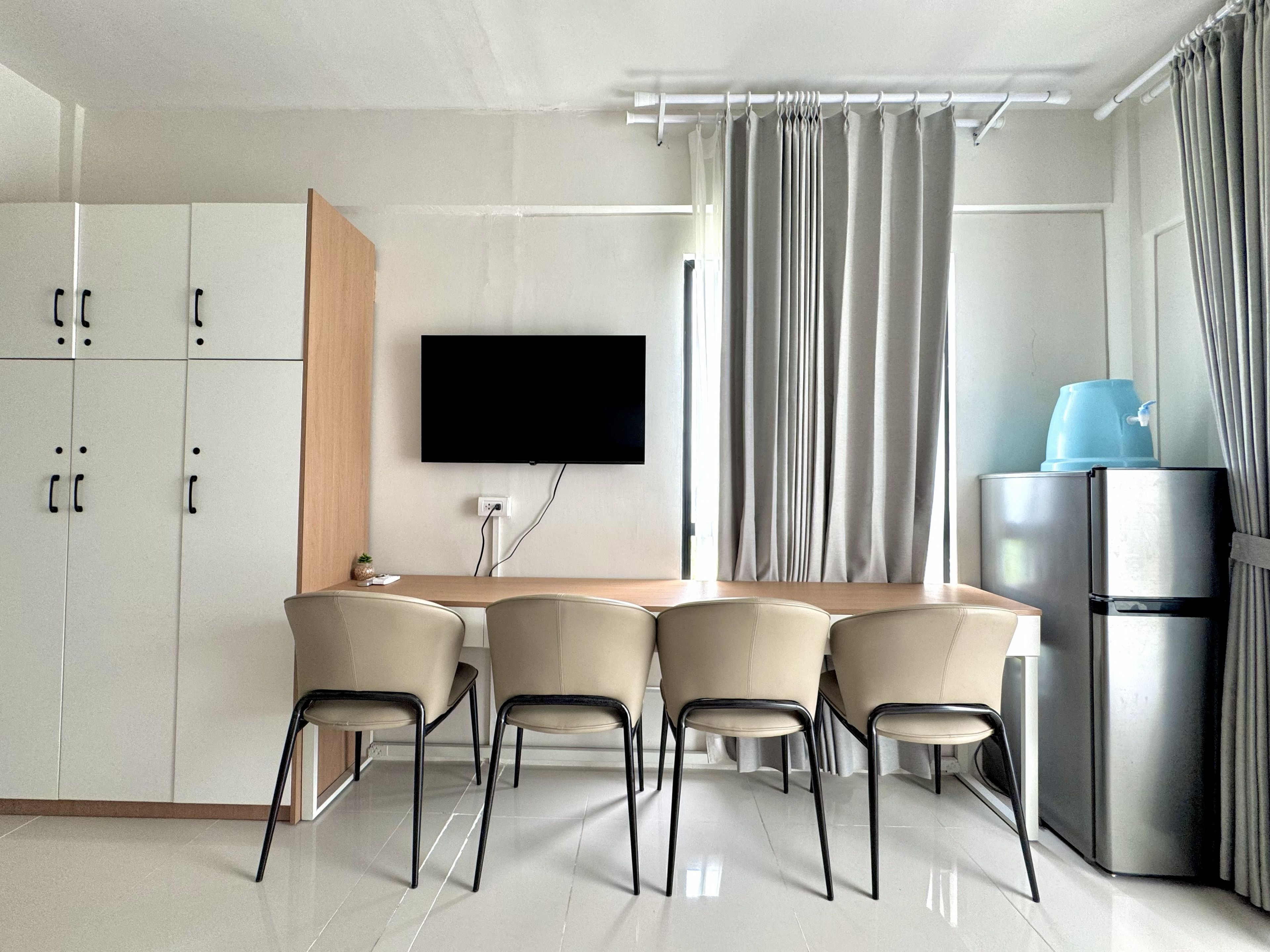 Una cocina moderna con televisor de pantalla plana, refrigerador y comedor con sillas.
