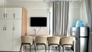 A modern kitchen with a flat-screen TV, a refrigerator, and a dining area with chairs. - Royal Oceancrest Panglao 1 (Dauis)