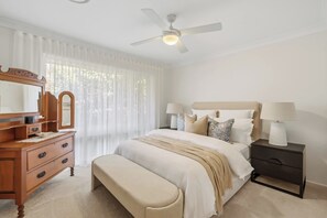 Ein Schlafzimmer mit einem Bett, Nachttischen, einer Kommode, einem Spiegel und einem Deckenventilator.
