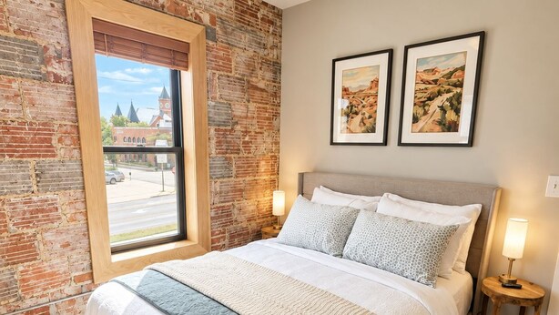 Una camera da letto con parete in mattoni, un letto grande, due abat-jour e due quadri appesi al muro.