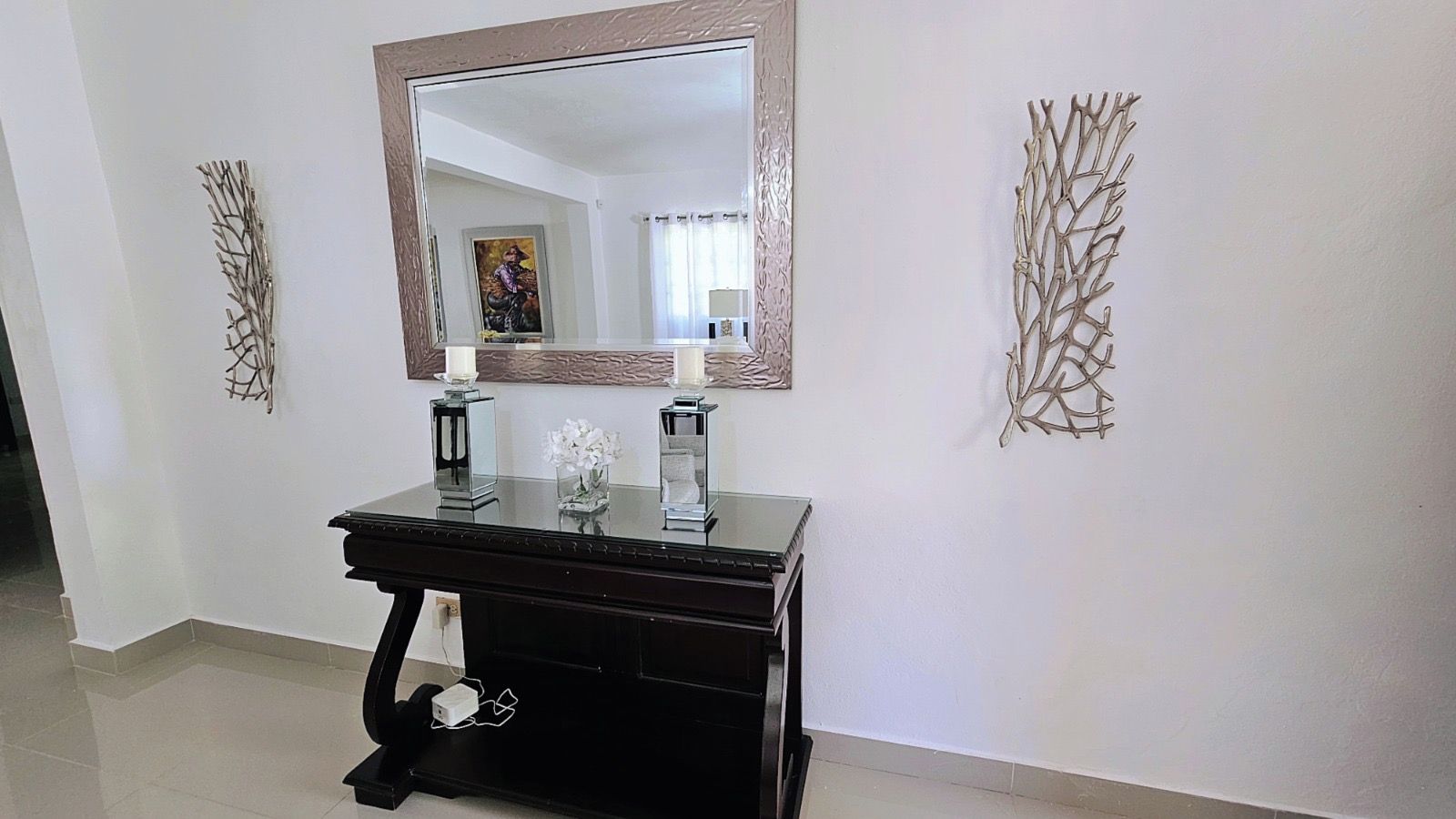 A black console table with a mirror above it, two candles, and a vase with white flowers.