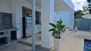 A modern outdoor kitchen area with a built-in grill, a refrigerator, and potted plants.