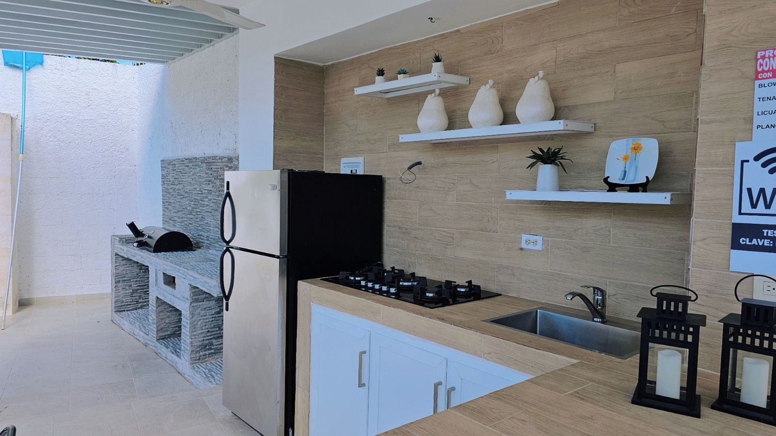 A modern kitchen with a built-in gas stove, a refrigerator, and a sink. There are decorative shelves with plants and a sign with text.
