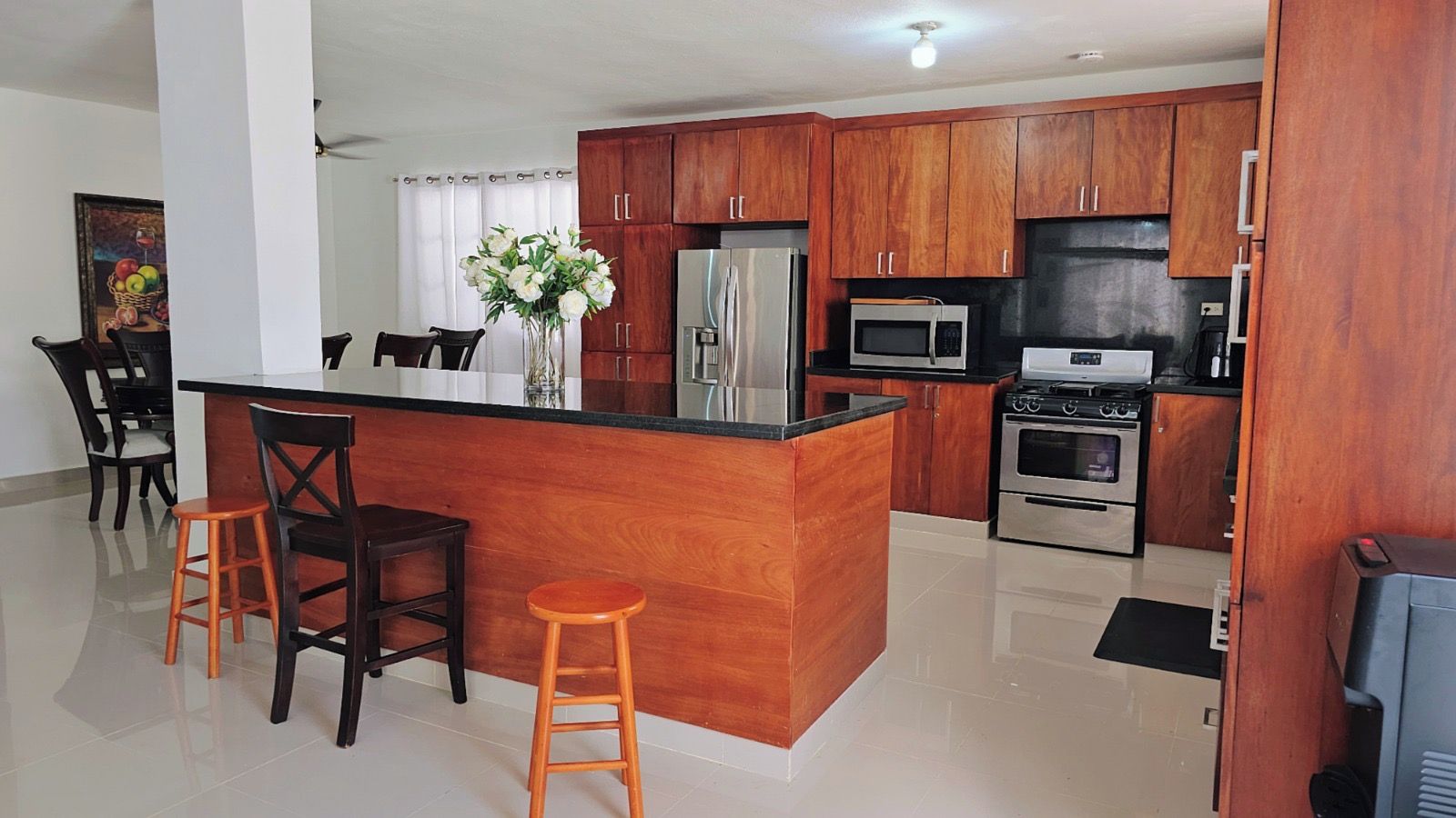 A modern kitchen with wooden cabinets, a central island, bar stools, and stainless steel appliances.