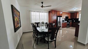 A dining area with a table and chairs, a kitchen with wooden cabinets, and a ceiling fan.