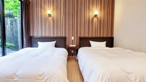 Habitación de hotel con dos camas, cabecera de madera, mesita de noche y ventana con cortinas.