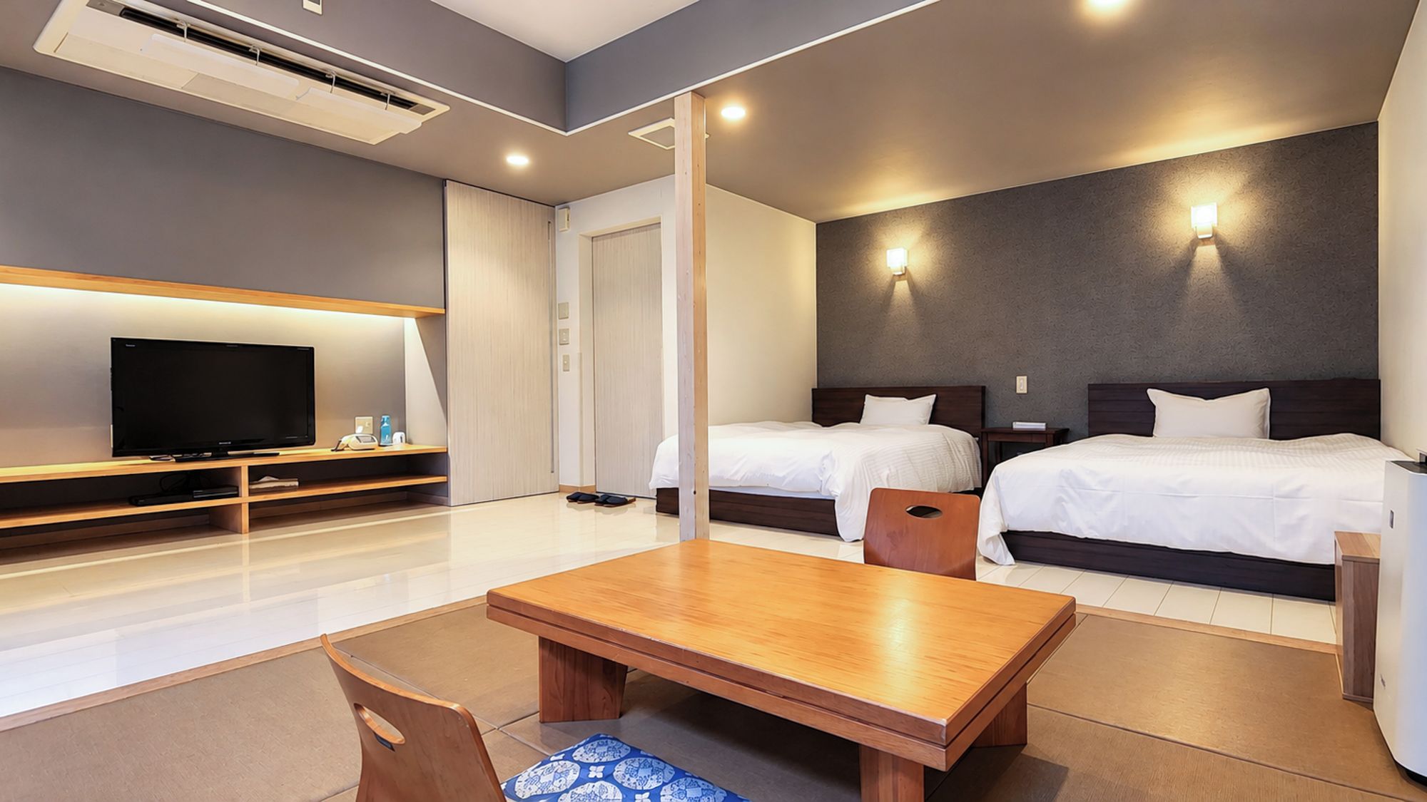 Une chambre d’hôtel moderne équipée d’un téléviseur à écran plat, de deux lits, d’une table en bois et d’une chaise.