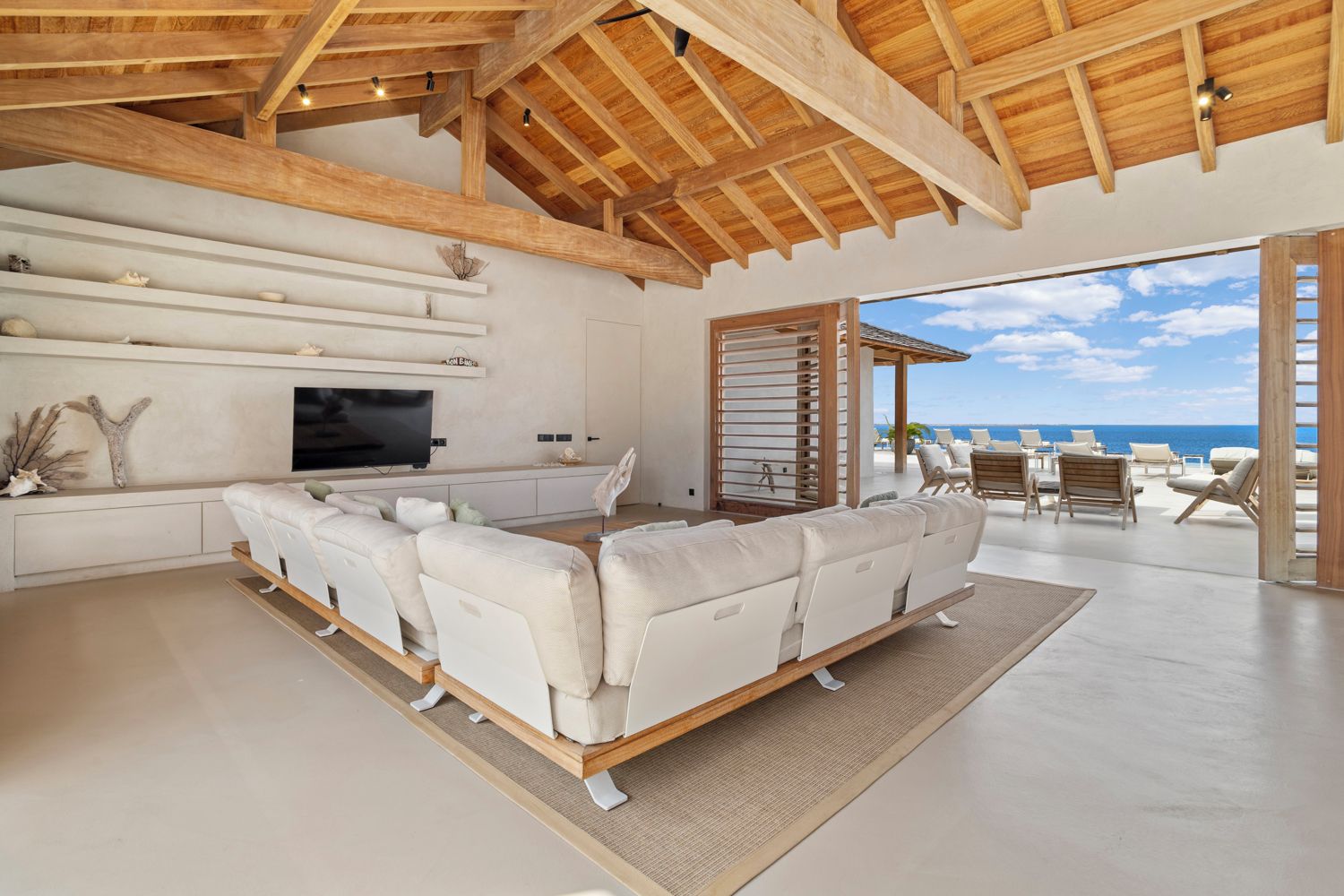 A modern living room with a large sofa, a flat-screen TV, and a view of the ocean.