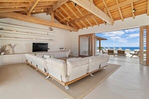 A modern living room with a large sofa, a flat-screen TV, and a view of the ocean.
