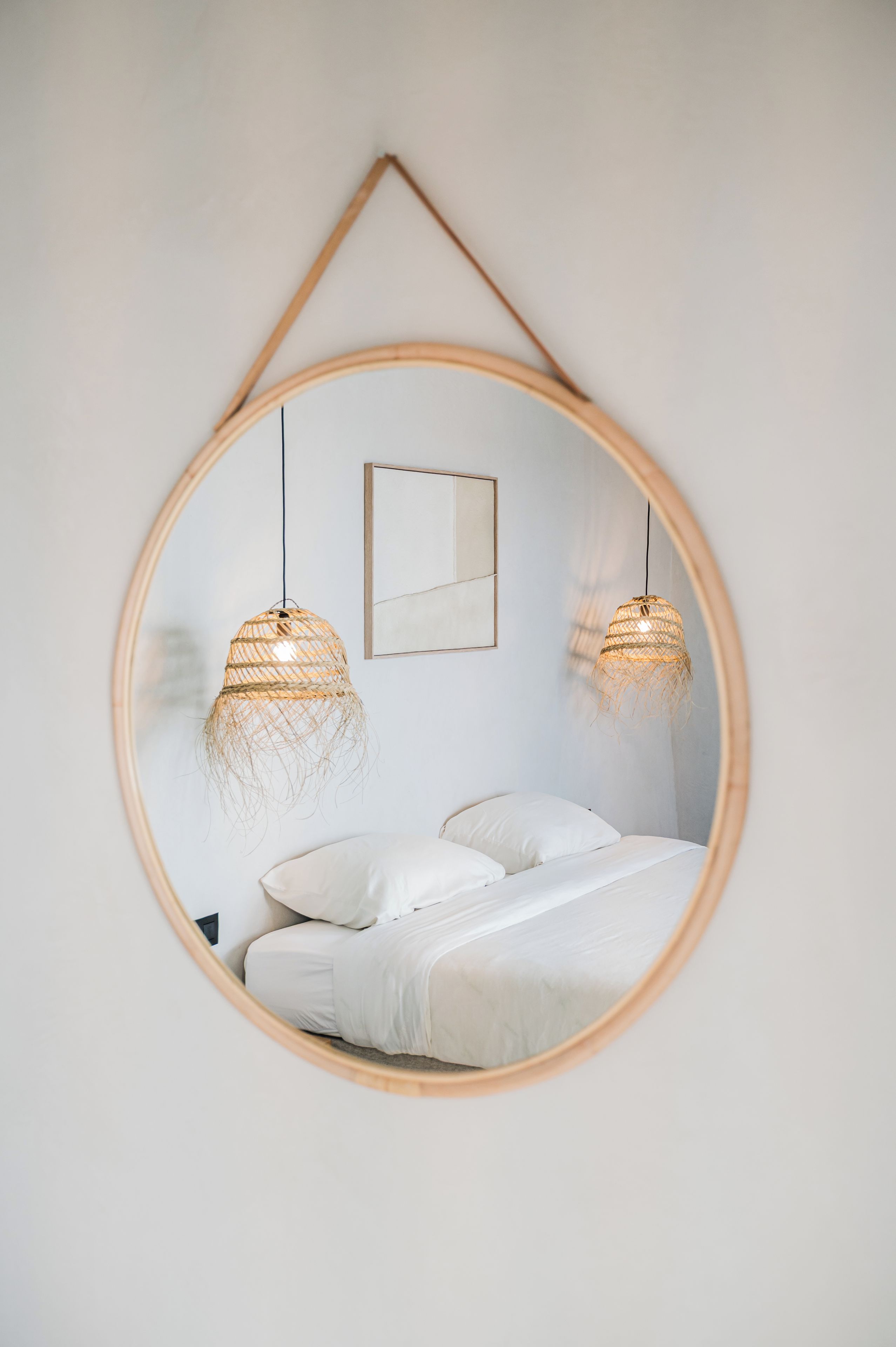 Un dormitorio con un espejo circular, dos lámparas colgantes, una cama y un cuadro en la pared.