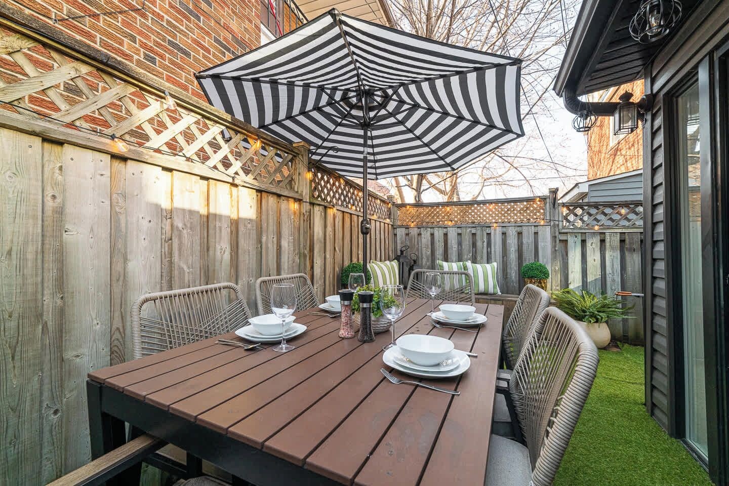 A wooden deck with a table set for dining, surrounded by wicker chairs and a striped umbrella.