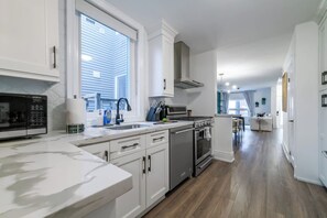 A modern kitchen with white cabinetry, a stainless steel stove, and a large window.