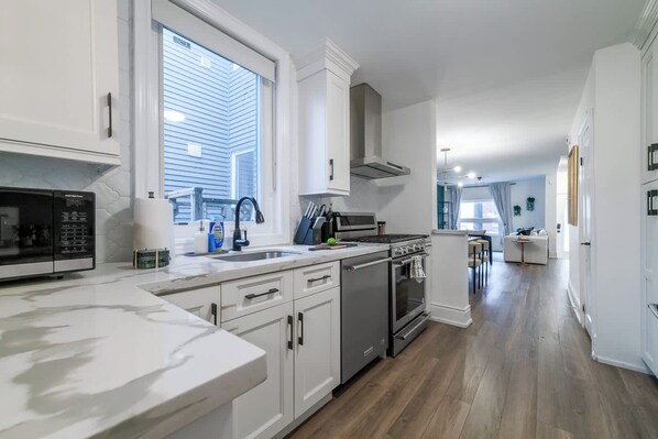 A modern kitchen with white cabinetry, a stainless steel stove, and a large window.