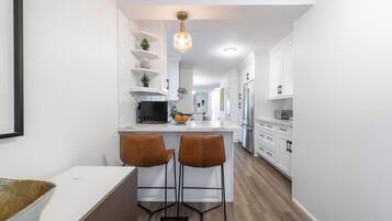 A modern kitchen with white cabinetry, a central island with bar stools, and a pendant light.
