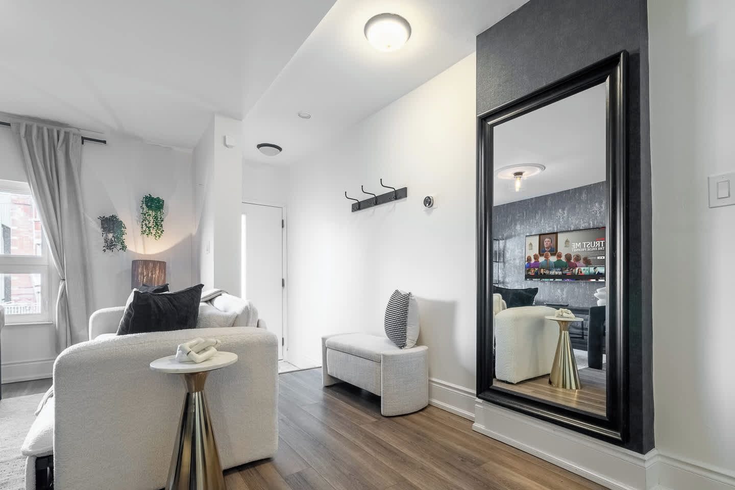 A modern living room with a large mirror, a sofa, a small table, and a view of the kitchen.