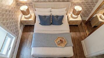 A bed with a headboard, two bedside tables with lamps, a bedside tray with a cup and nuts, and a window.