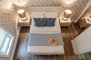 A bed with a headboard, two bedside tables with lamps, a bedside tray with a cup and nuts, and a window.