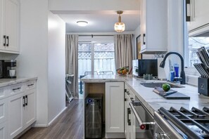 A modern kitchen with a built-in oven, a stainless steel range hood, and a window overlooking a balcony. - Chic Ossington Escape 3BR w Patio in Downtown (Toronto)