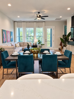 A dining area with a table set for four, surrounded by teal chairs, a ceiling fan, and a view of the outdoors through large windows. - Modern Charlotte Retreat - Sleeps 10 - Near UNCC & Uptown (Charlotte)