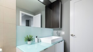 Un baño moderno con cubierta de vidrio, lavamanos blanco y armarios de madera oscura.