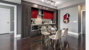 Una cocina moderna con armarios oscuros, una pared de acento roja y una mesa de comedor de vidrio con sillas.
