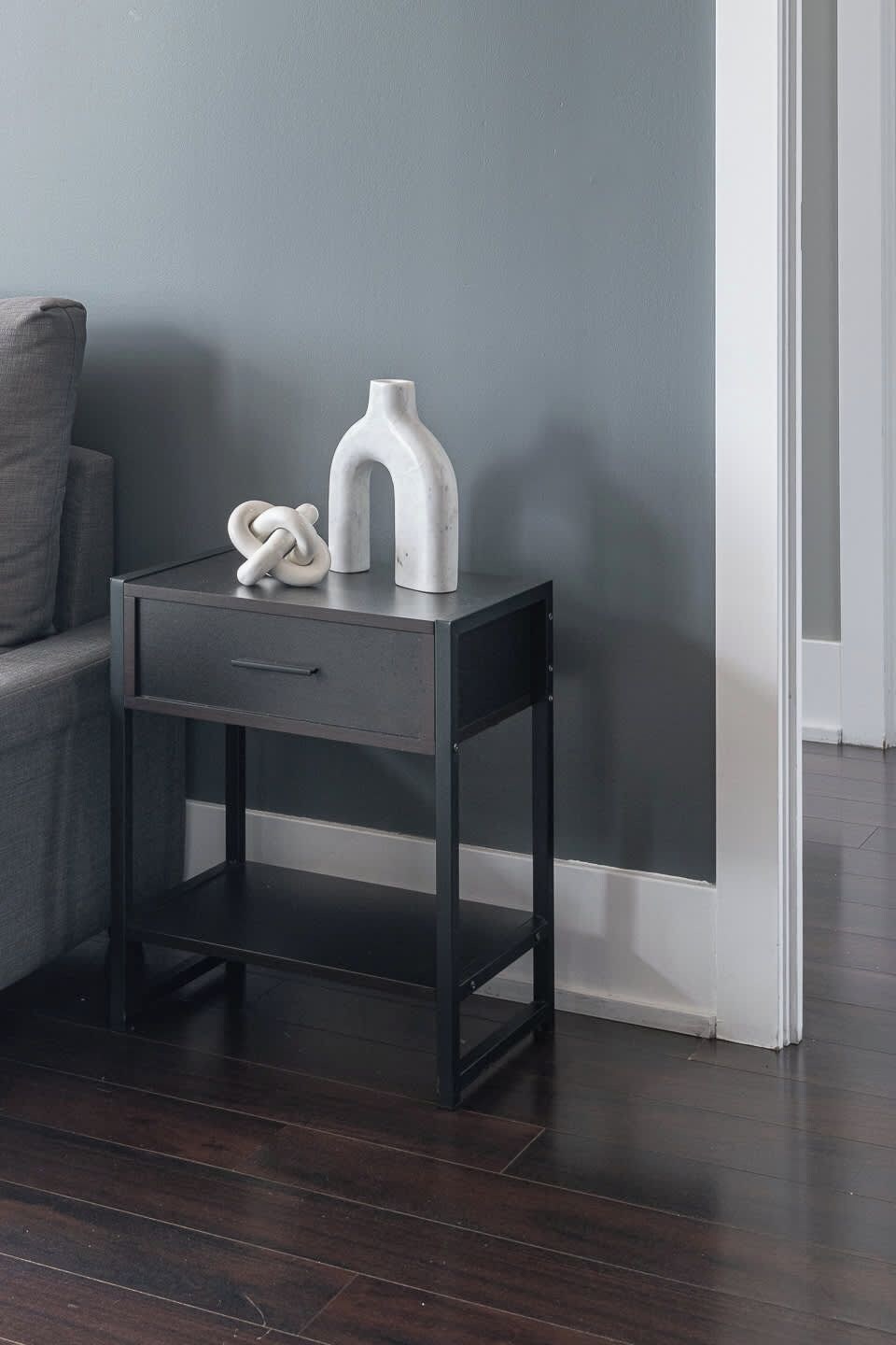 A dark wooden nightstand with a drawer and shelves, against a grey wall.