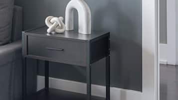 A dark wooden nightstand with a drawer and shelves, against a grey wall.