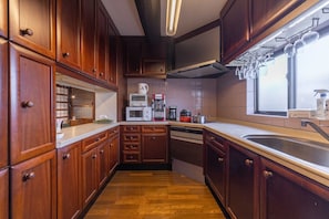 A compact kitchen with wooden cabinets, a microwave, a coffee maker, and a window with hanging glasses.