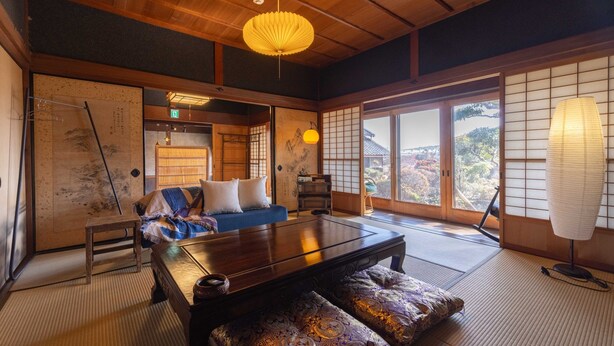Um quarto japonês tradicional com piso de tatame, uma mesa de madeira baixa e vista para um jardim através de uma porta deslizante.