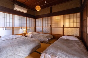 A traditional Japanese-style room with tatami flooring, a futon bed, a hanging lamp, and a sliding shoji screen.