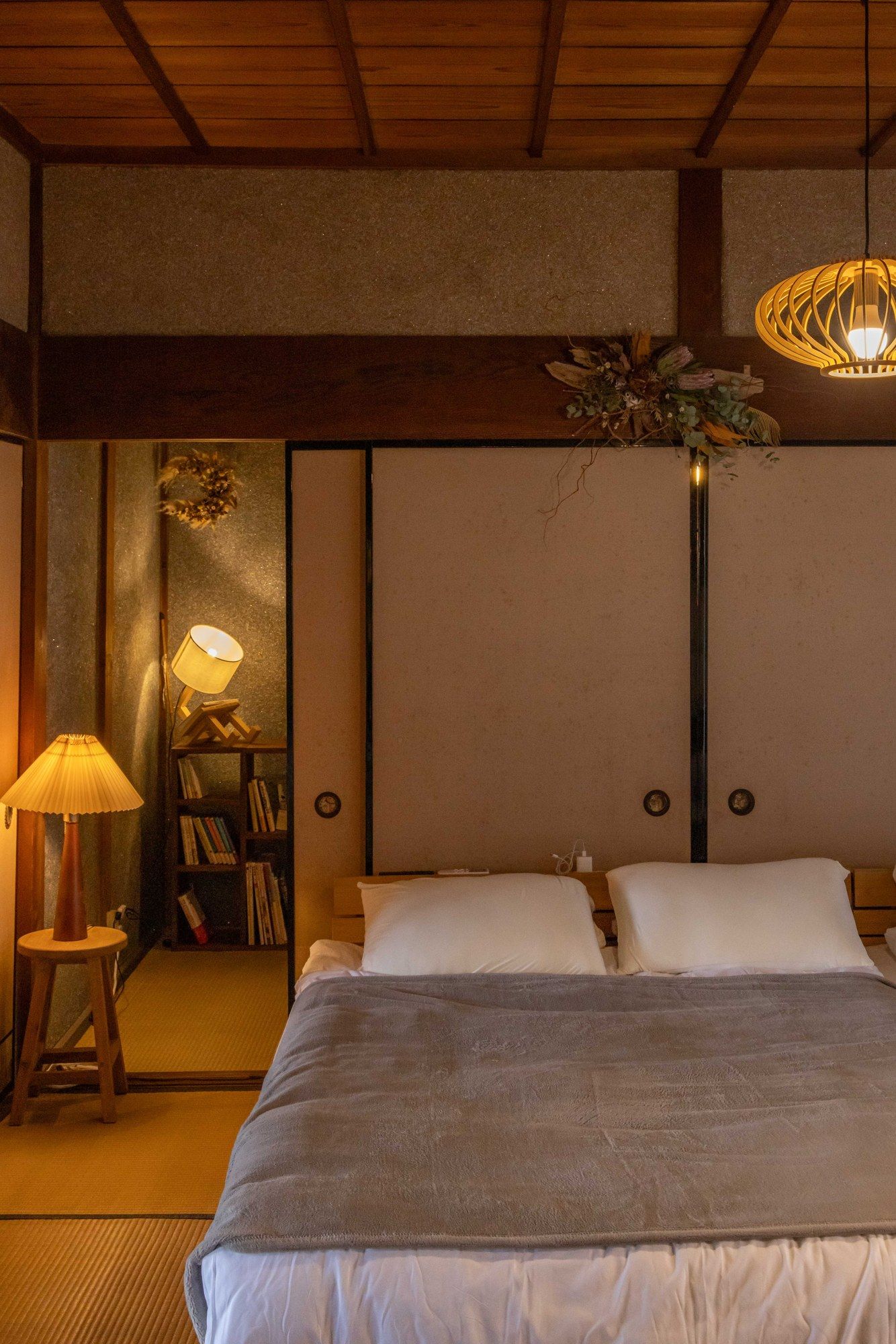 A bedroom with a bed, a nightstand, a lamp, and a bookshelf.