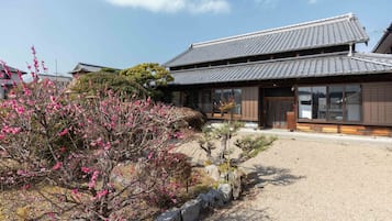 A traditional Japanese building with a tiled roof, a gravel driveway, and a garden with flowering trees.
