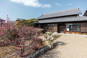 A traditional Japanese building with a tiled roof, a gravel driveway, and a garden with flowering trees.